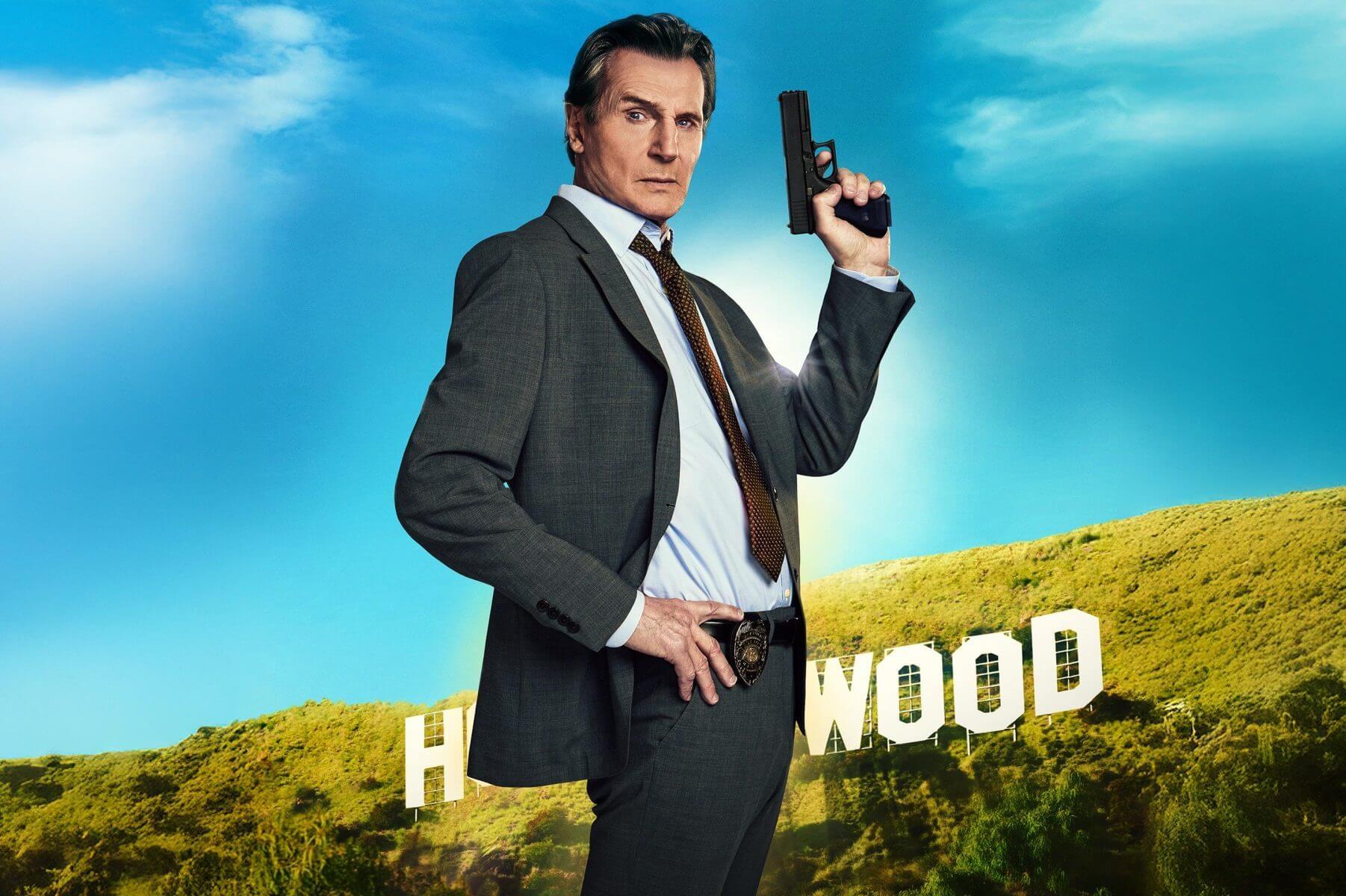 Liam Neeson como Frank Drebin Jr. sosteniendo una pistola frente al cartel de Hollywood en ¿Y dónde está el policía 2025?