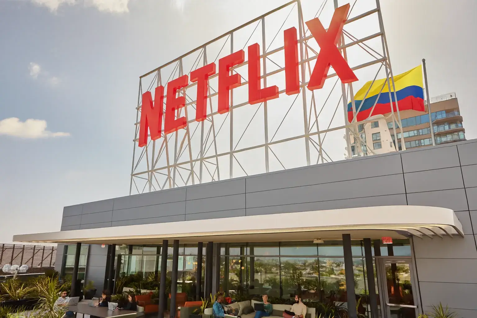 Fachada de Netflix con una gran bandera de Colombia ondeando junto al logo, representando la llegada de series colombianas en Netflix.