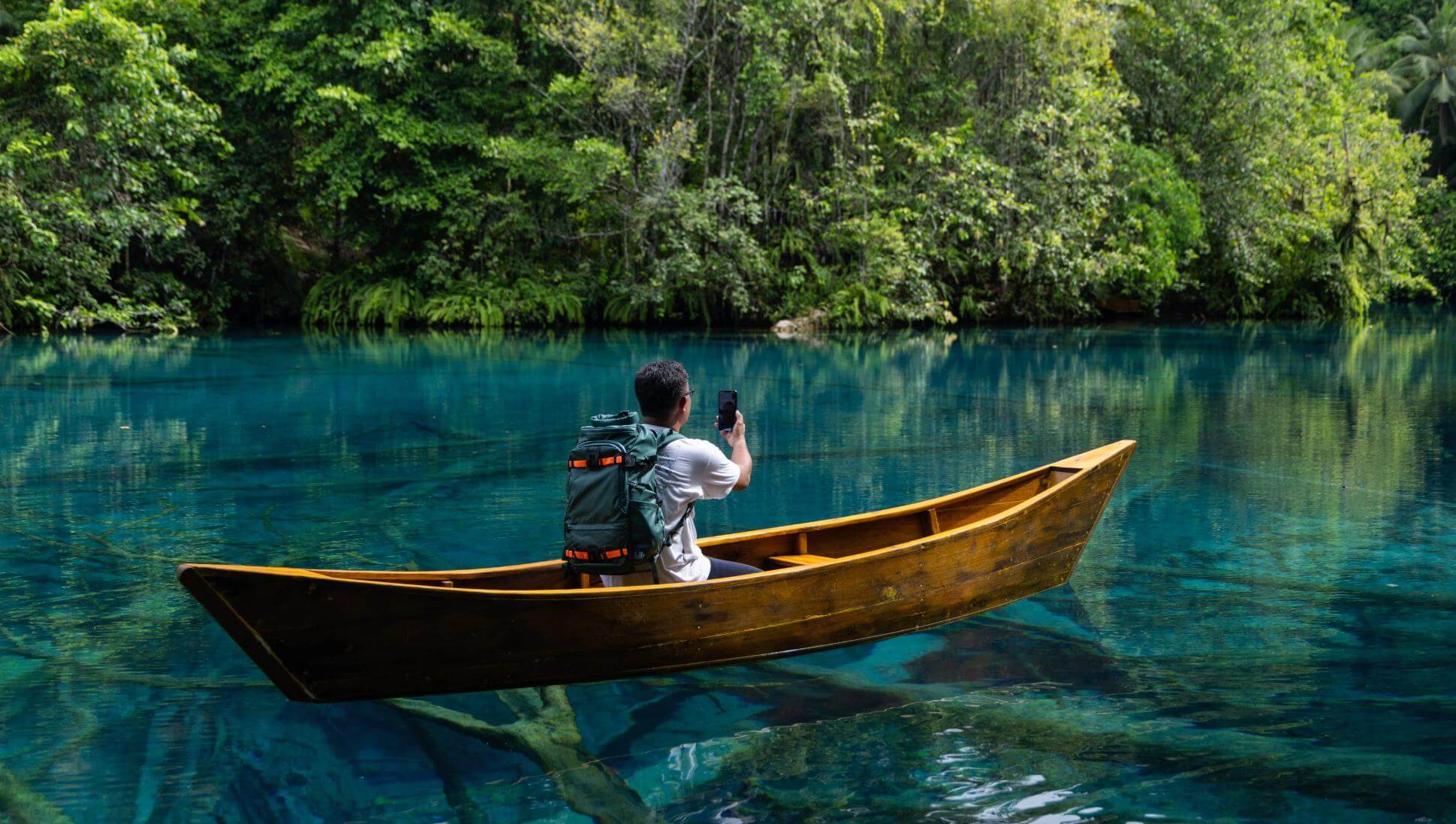 Hombre en una canoa de madera usando su teléfono móvil en medio de una laguna cristalina rodeada de selva, representando la conectividad de Starlink Direct to Cell en lugares remotos