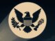 Emblema del águila de Estados Unidos proyectado como señal en el cielo, evocando la “Bati-señal”, en referencia al apodo de Christopher Landau el quita visas