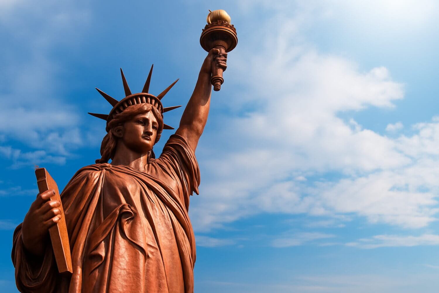 La Estatua de la Libertad en su color original de cobre rojizo, mostrando la textura metálica y el verdadero color de la Estatua de la Libertad contra un cielo azul con nubes