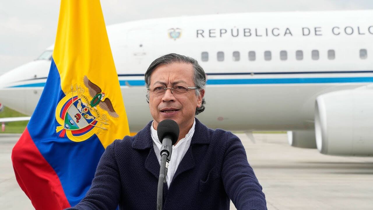 El presidente Gustavo Petro ofrece una alocución frente a un micrófono, con la bandera de Colombia a su lado y un avión oficial con la inscripción “República de Colombia” de fondo, en el contexto de la descertificación de Colombia
