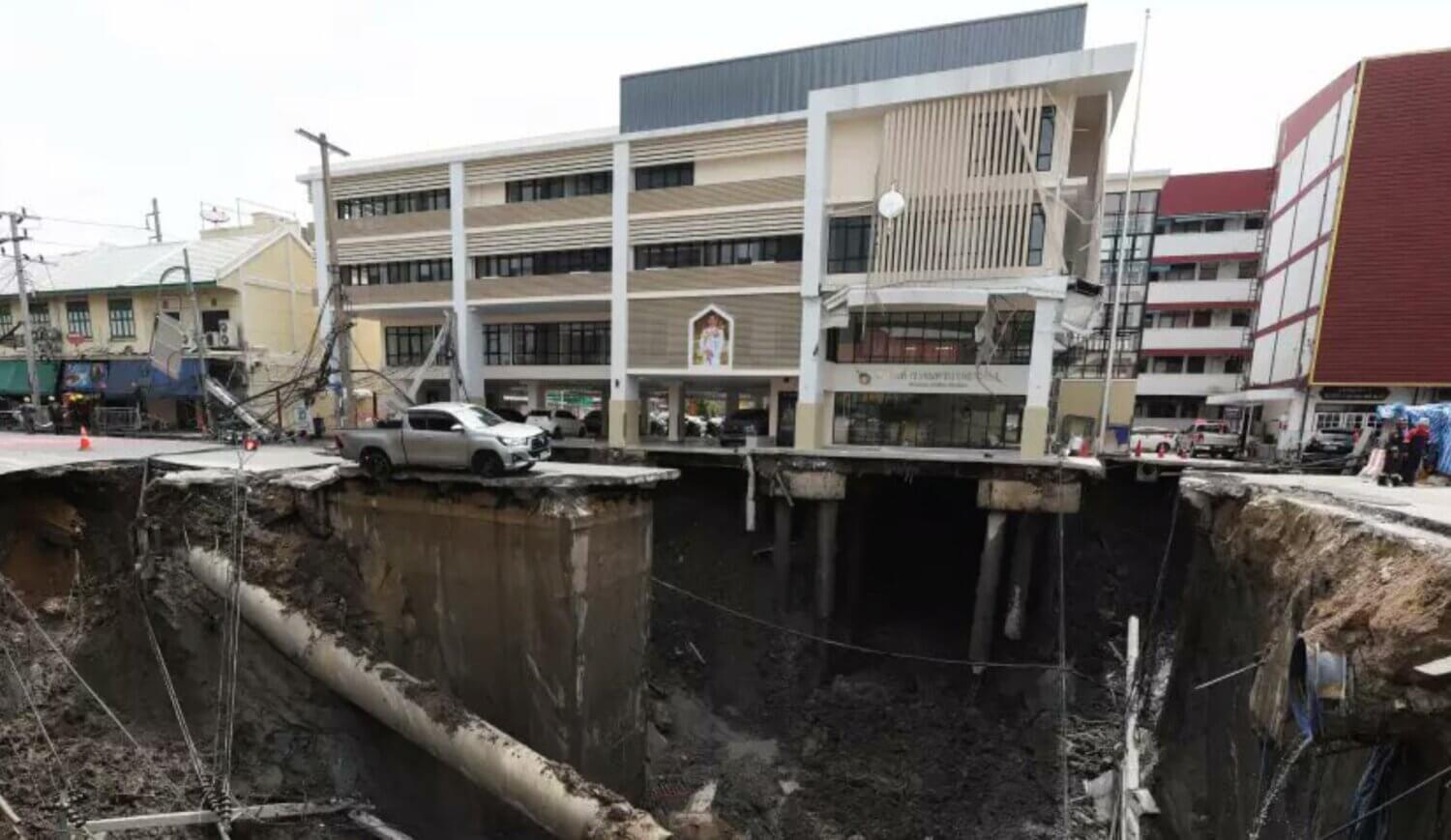 Vista del enorme socavón en Tailandia frente a un hospital en Bangkok, con un vehículo al borde del hundimiento y postes eléctricos colapsados