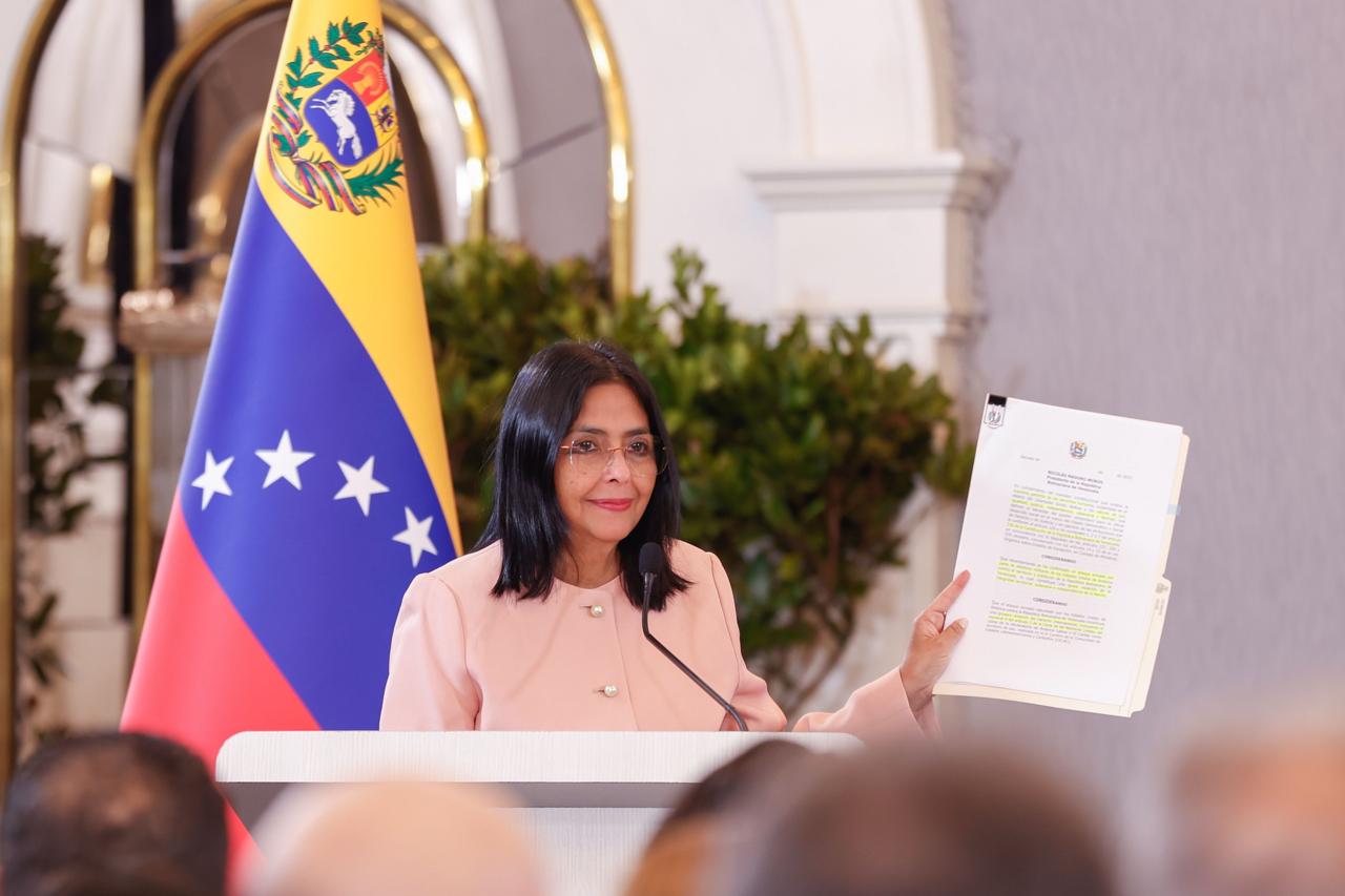 La vicepresidenta de Venezuela, Delcy Rodríguez, sostiene un documento oficial durante un discurso, con la bandera venezolana de fondo, al anunciar el Estado de Conmoción Externa