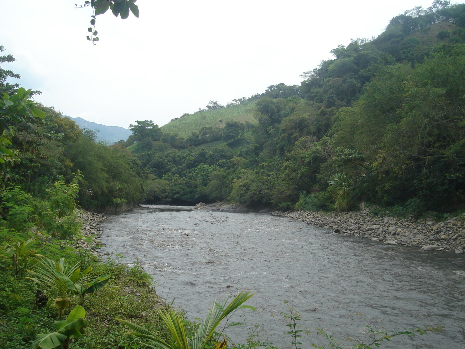 Laguna Larga en Villeta, cuerpo de agua rodeado de vegetación y montañas, con orillas de piedras y un ambiente natural de contemplación