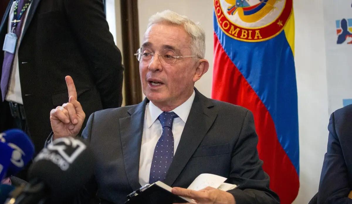 Álvaro Uribe Vélez habla ante medios de comunicación con la bandera de Colombia al fondo