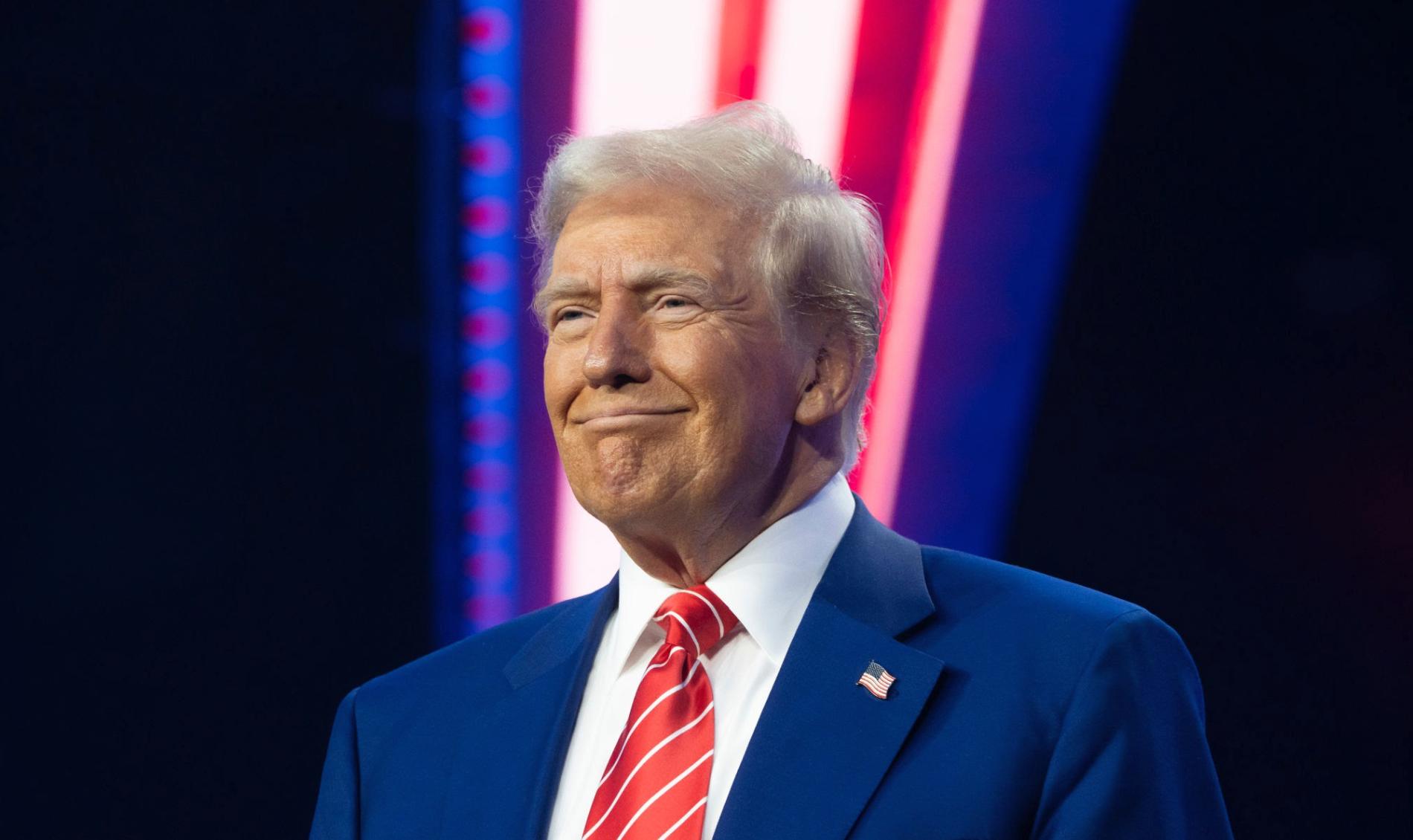 El presidente Donald Trump sonríe en un escenario iluminado con luces rojas y azules, tras anunciar su ultimátum para alcanzar la paz en Medio Oriente