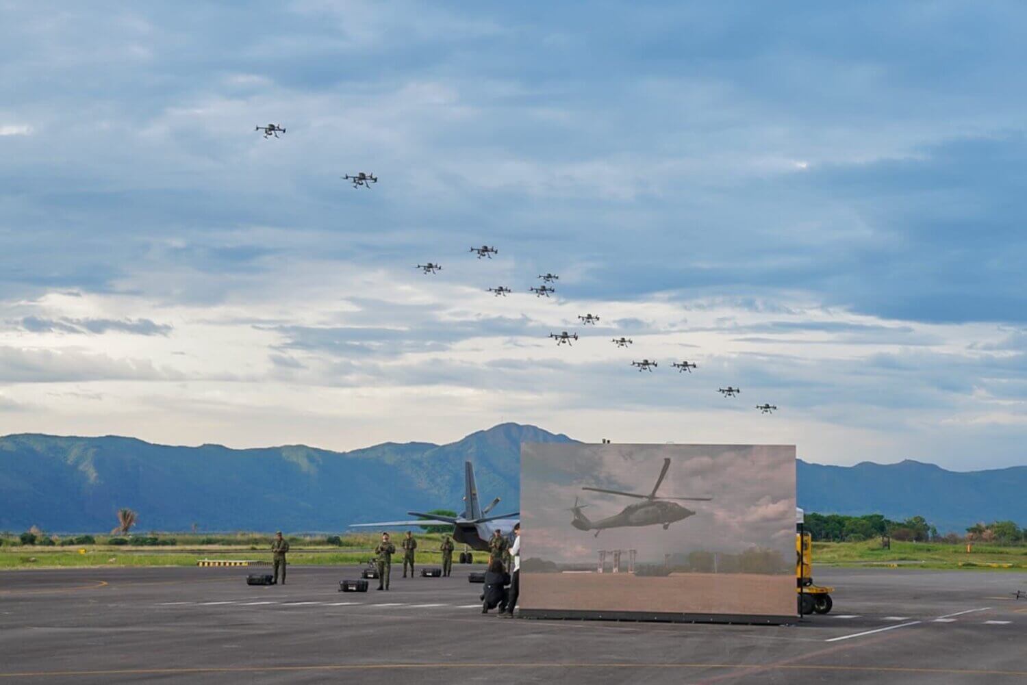 Formación de drones volando sobre una pista militar en Colombia durante la activación del nuevo batallón de drones, con soldados en tierra y montañas al fondo