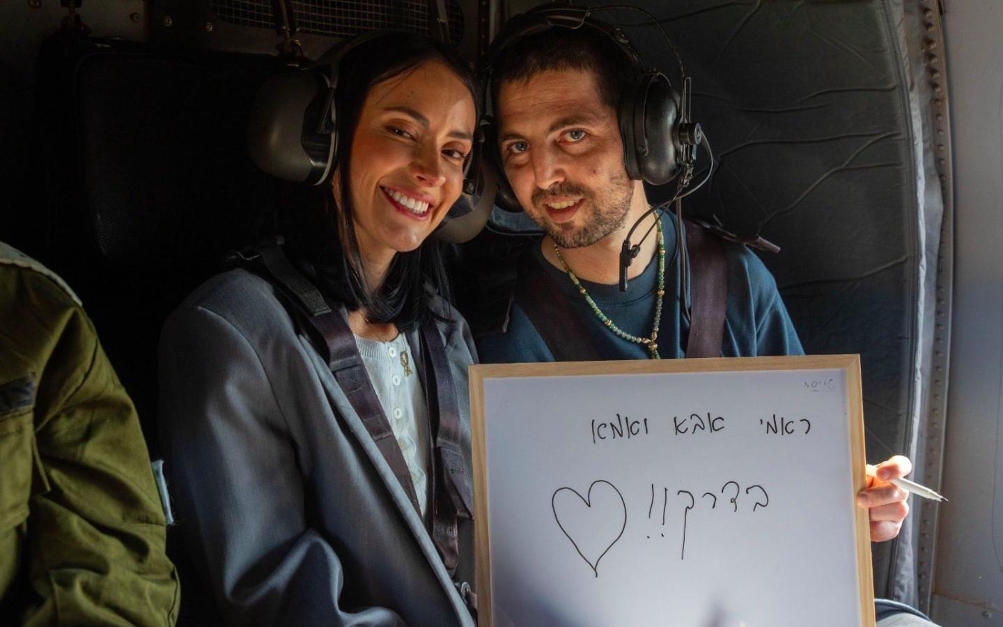 El colombiano liberado en Gaza, Elkana Bohbot, sonríe junto a su esposa Rebecca González a bordo de un helicóptero tras su liberación, sosteniendo una pizarra con un mensaje de agradecimiento en hebreo
