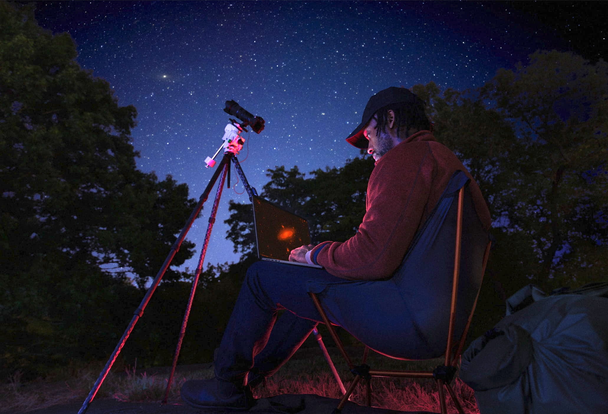Persona trabajando de noche con un MacBook Pro bajo un cielo estrellado, acompañado de un telescopio, ilustrando la autonomía del MacBook Pro con chip M5 durante largas jornadas al aire libre