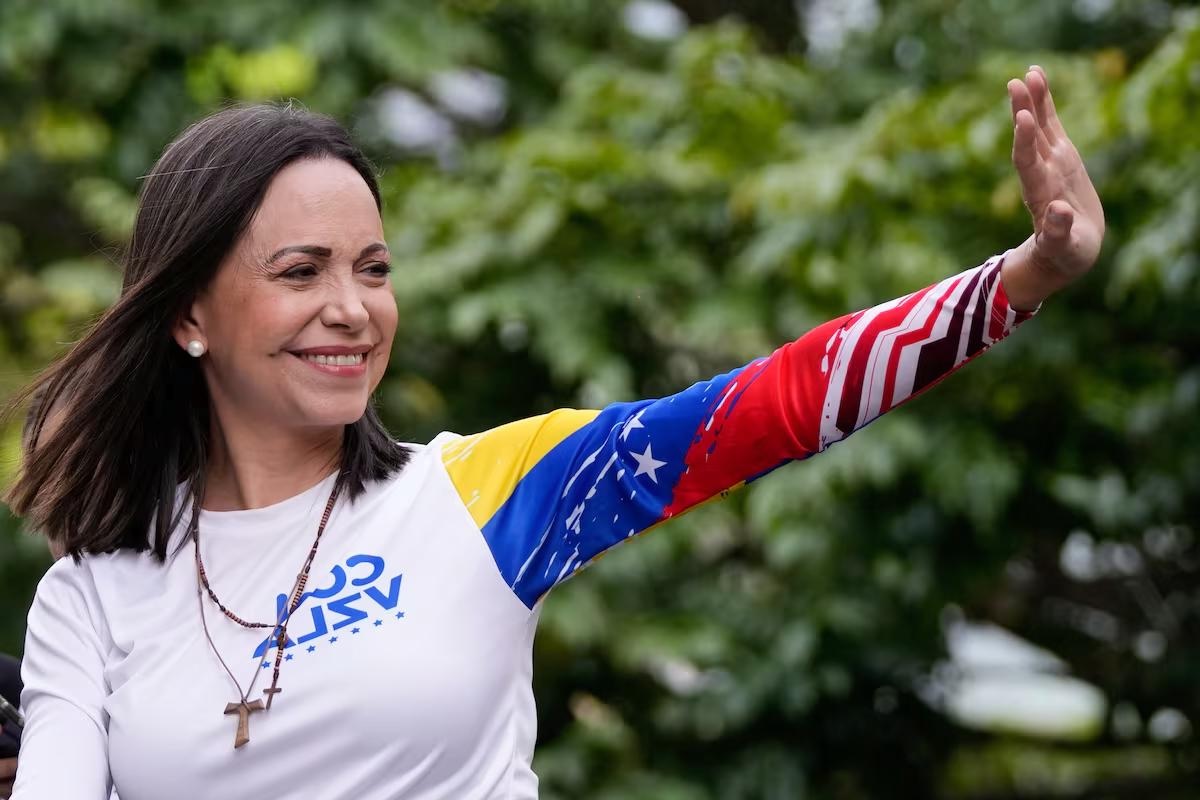 María Corina Machado sonríe y saluda durante un acto público en Venezuela, tras recibir el Nobel de la Paz 2025, vistiendo una camiseta con los colores de la bandera nacional