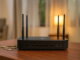 Router inalámbrico moderno sobre una mesa de madera con monedas al costado, representando los cobros por reconexión en servicios de telecomunicaciones