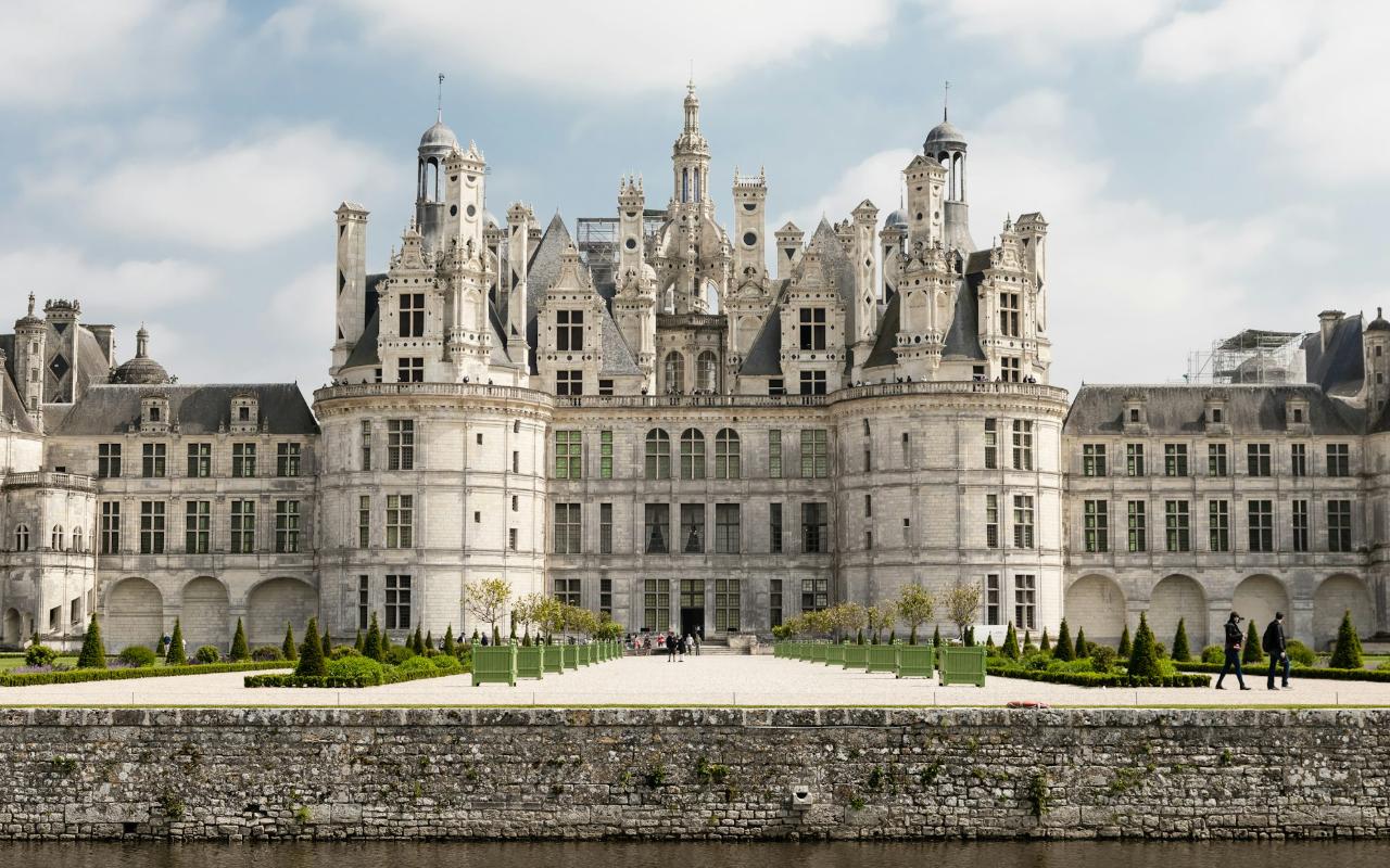 Fachada frontal de un majestuoso castillo europeo rodeado de jardines y un canal, símbolo del esplendor de los países que aún tienen reyes o reinas.