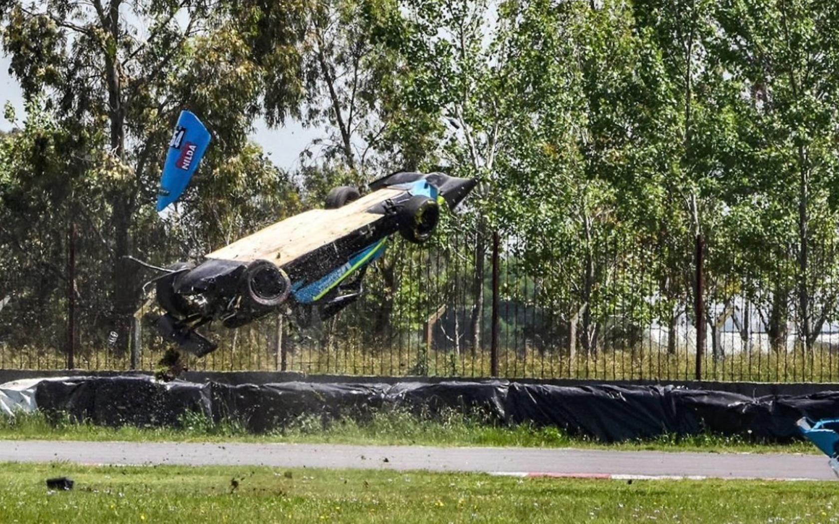 Vista del monoplaza Crespi de Mariano Morini volando por el aire durante el accidente de Mariano Morini en la Fórmula 4 en el Autódromo Mouras de La Plata, con una de las piezas desprendiéndose y el auto dado vuelta en pleno impacto