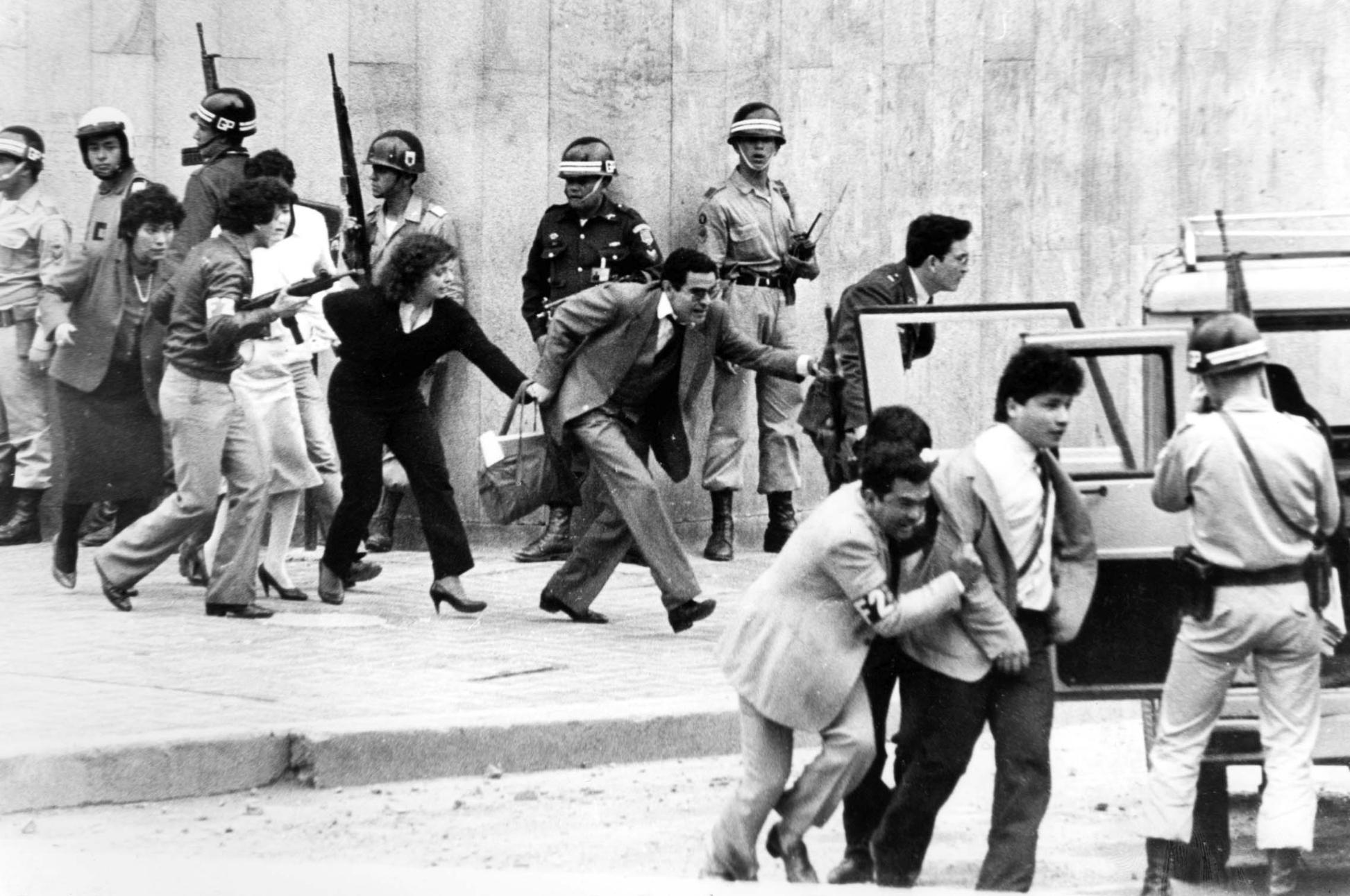 Civiles y rehenes evacúan el Palacio de Justicia bajo custodia militar durante la toma de 1985, mientras soldados del Ejército contienen la situación en medio de las exigencias del M-19 en el Palacio de Justicia