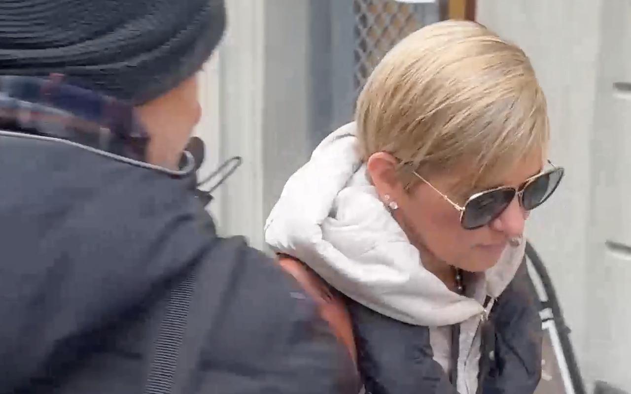 Verónica Alcocer en Estocolmo caminando con gafas oscuras y abrigo claro, acompañada de un hombre que intenta cubrir la cámara mientras avanzan por una calle comercial