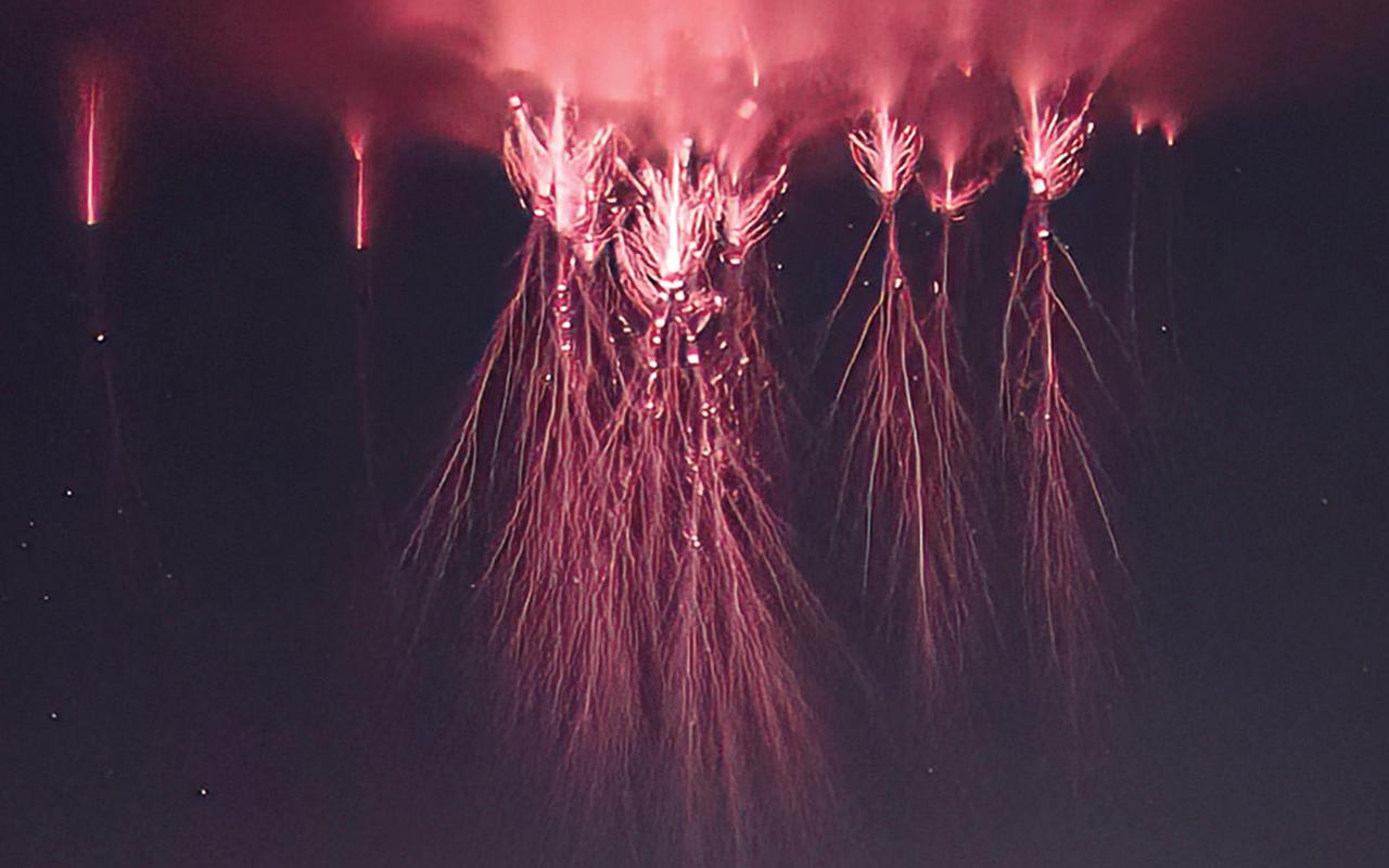 Duendes rojos visibles como múltiples descargas eléctricas de color rojo intenso, con filamentos luminosos que descienden desde la atmósfera superior sobre una tormenta nocturna, formando estructuras verticales ramificadas en el cielo oscuro