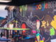 Interior de la oficina de Google en Bogotá, con una pared decorada con ilustraciones coloridas y la palabra ‘Google Bogotá’, junto a una fotografía de una calle tradicional con montañas al fondo