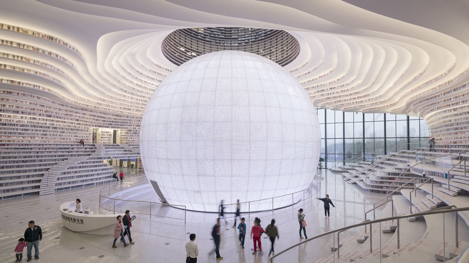 Interior futurista de la Biblioteca de Tianjin Binhai en China, con una enorme esfera central luminosa rodeada de estanterías onduladas y visitantes recorriendo el espacio, simbolizando la potencia cultural de China